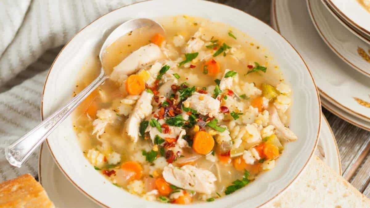 A bowl of chicken noodle soup with carrots and bread.