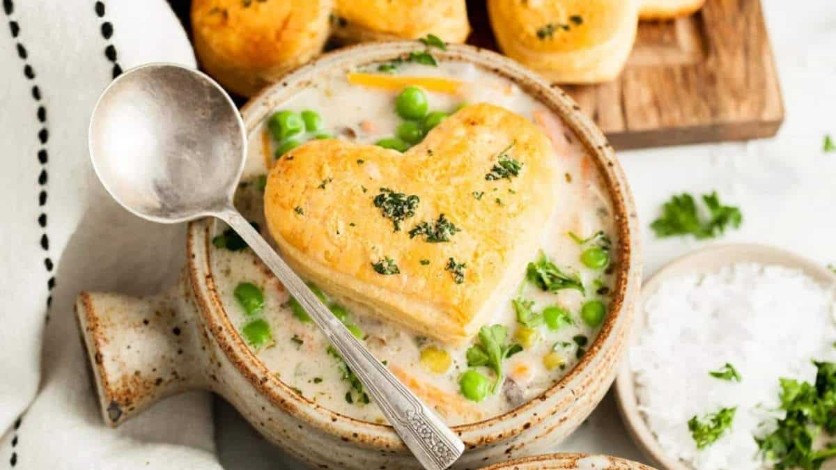 A heart shaped bowl of soup with biscuits and peas.