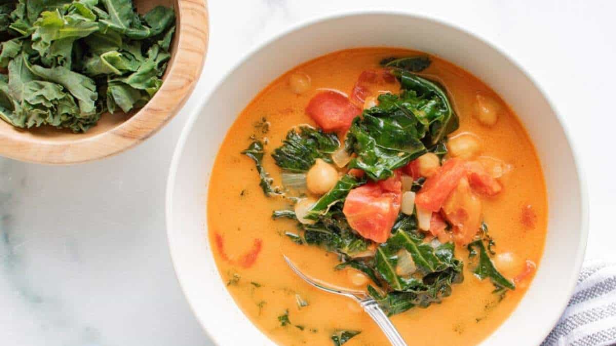 A bowl of tomato and kale soup with a spoon. This delicious recipe for tomato and kale soup is sure to warm you up on a chilly day. Enjoy the comforting flavors of ripe tomatoes and