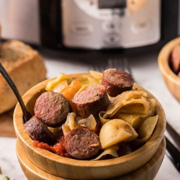 A bowl of pasta with sausage served alongside bread, perfect for a hearty meal.