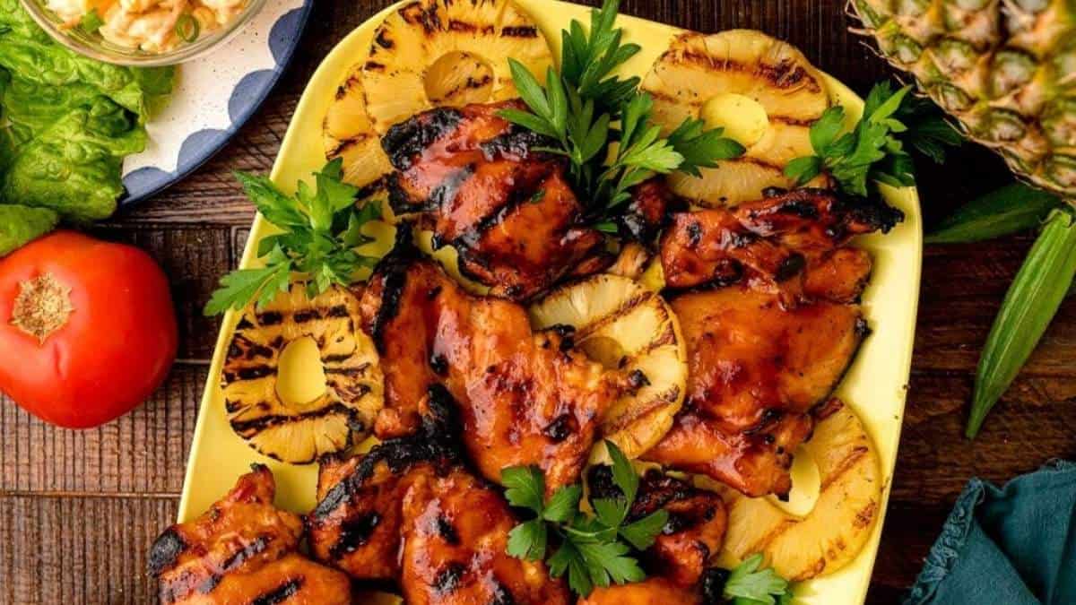 Hawaiian chicken skewers on a plate with pineapples and tomatoes.