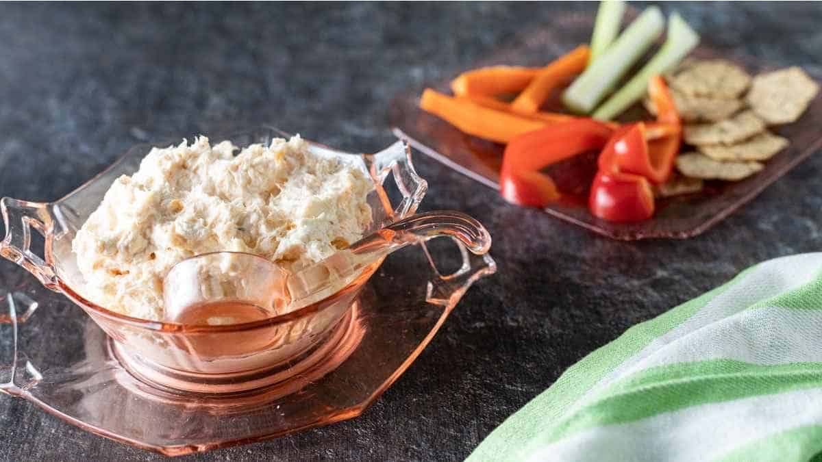 A bowl of dip with crackers and vegetables.