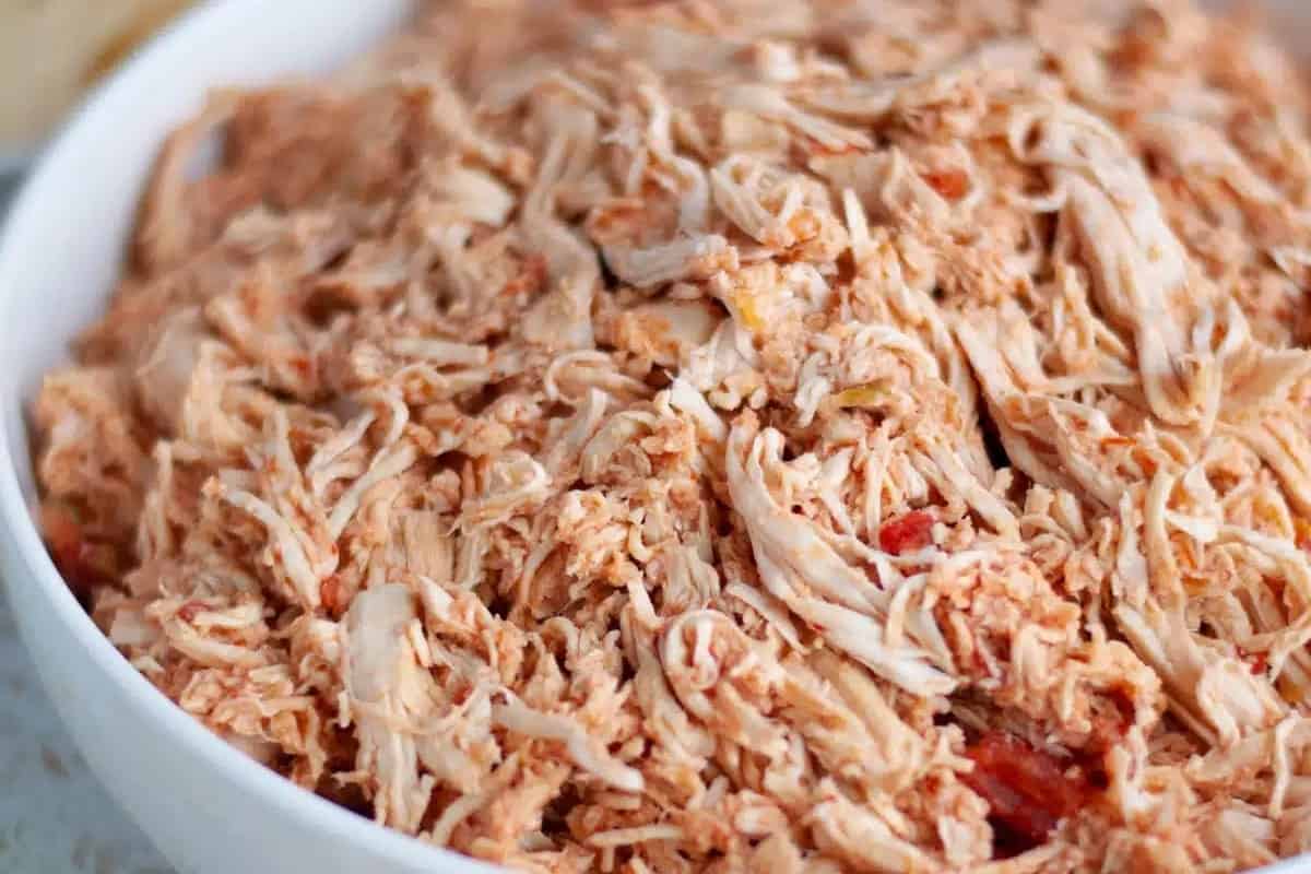 Shredded chicken in a white bowl on a table.
