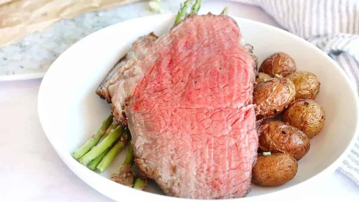 A white bowl with a steak, potatoes and asparagus.