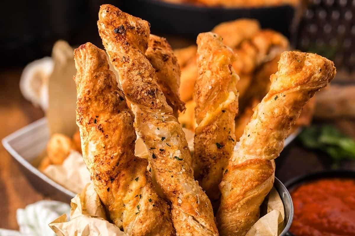 Cheesy garlic bread sticks in a basket on a wooden table.