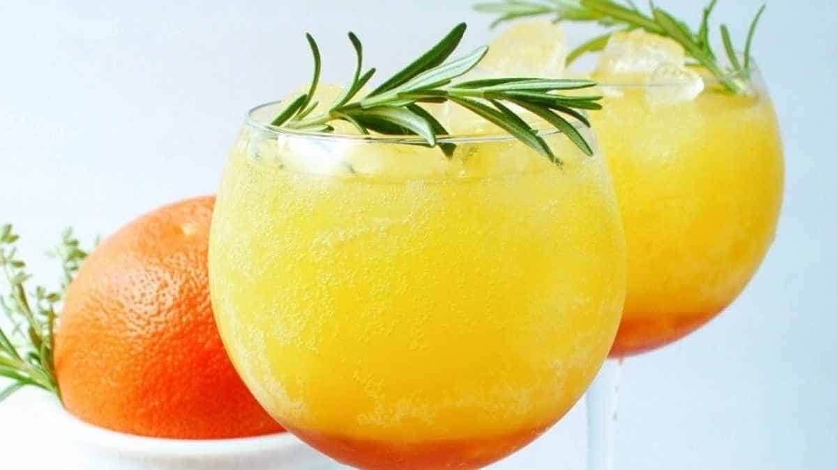 Two glasses of orange juice with rosemary sprigs.