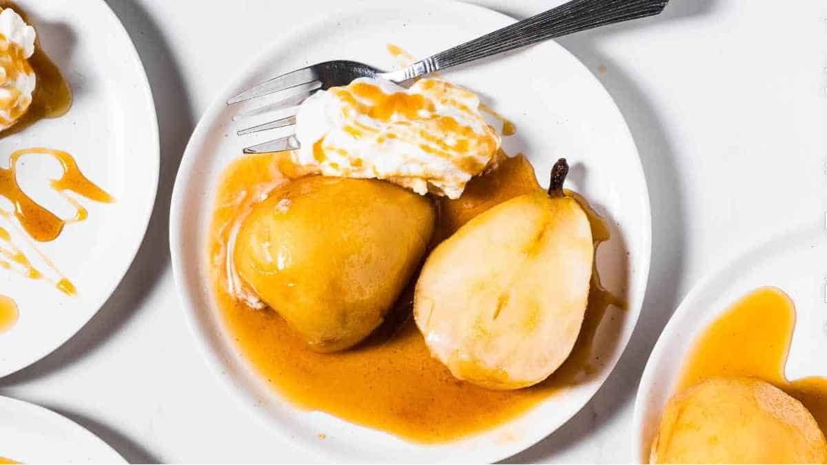 Pears with caramel sauce and whipped cream on a white plate.
