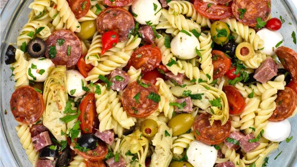 A bowl of pasta salad with meat, tomatoes and olives.