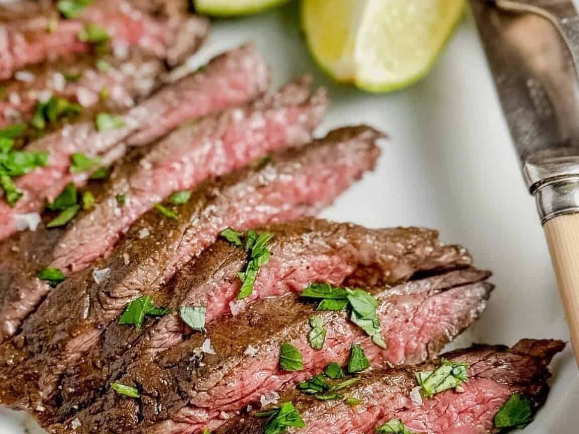 Steak on a white plate with lime wedges.