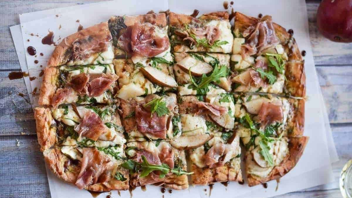 A pizza with apples and ham on top.