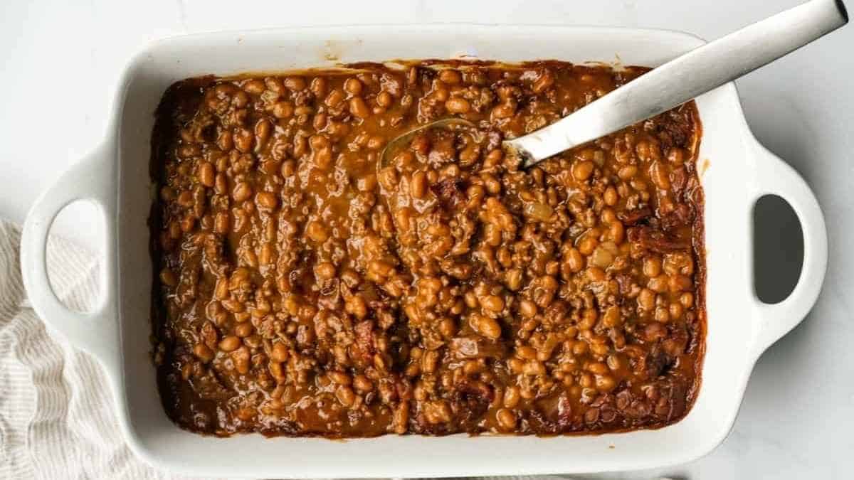Baked beans in a white casserole dish with a spoon.