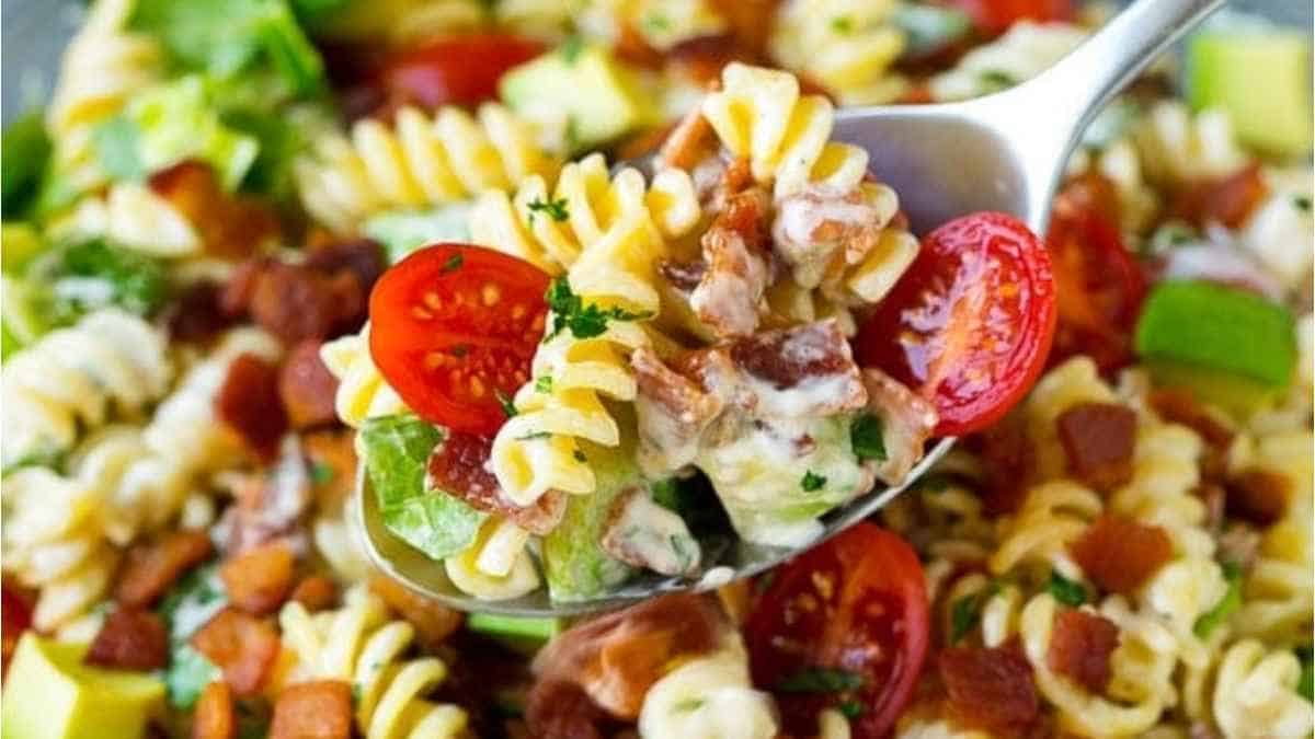 A spoon full of pasta salad with bacon and tomatoes.