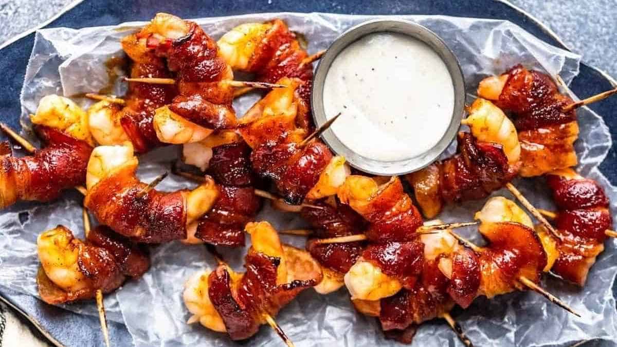 Bacon wrapped shrimp on skewers with dipping sauce.