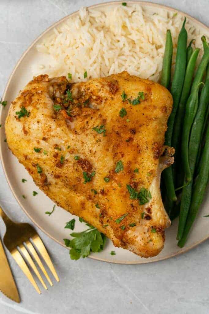 Chicken thighs on a plate with rice and green beans.
