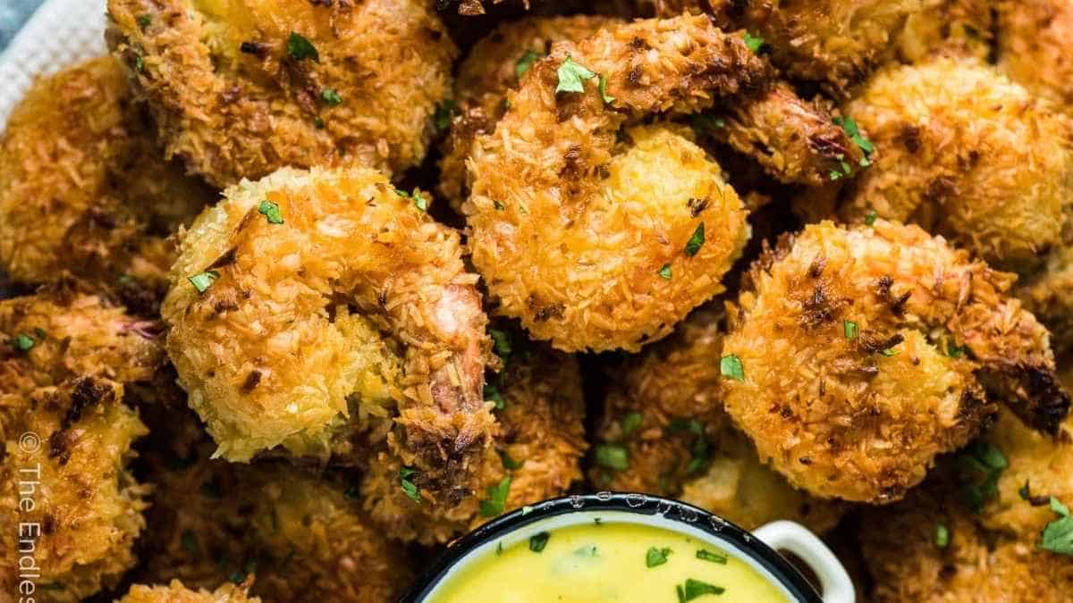 Fried coconut shrimp with dipping sauce on a plate.