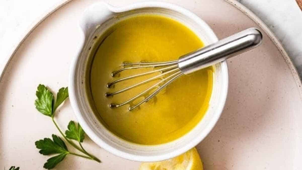 A bowl of lemon dressing with a whisk and parsley.