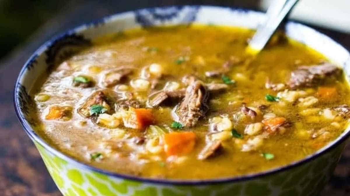 A bowl of beef and barley soup with a spoon.