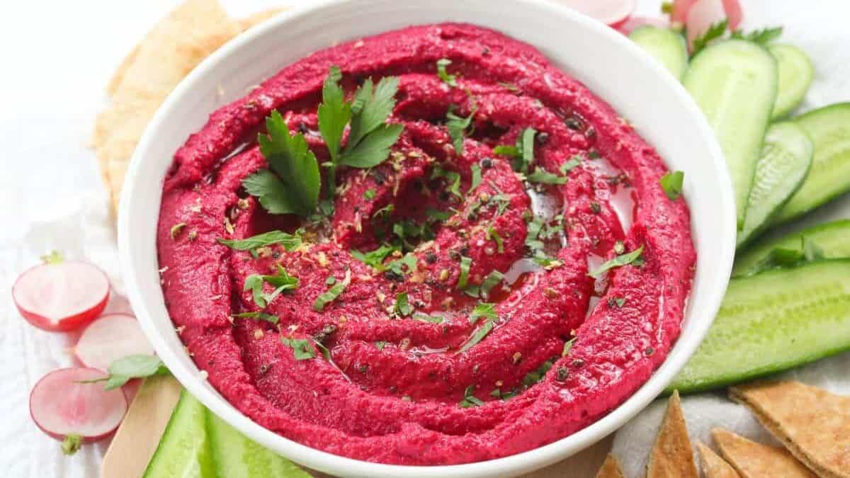 A bowl of beet hummus with cucumbers and radishes.