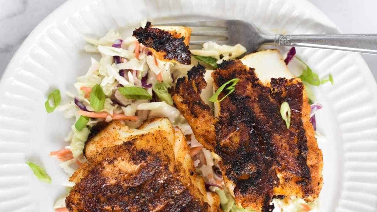 A plate of grilled fish with coleslaw and a fork.