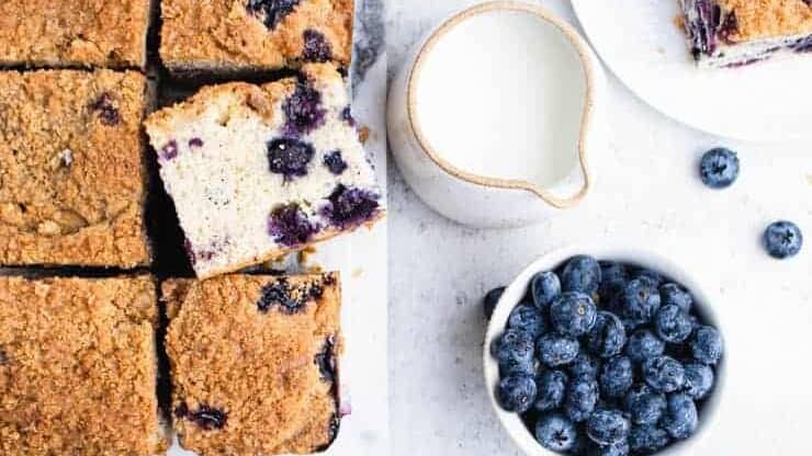A blueberry cake with blueberries in a bowl and a bowl of milk.