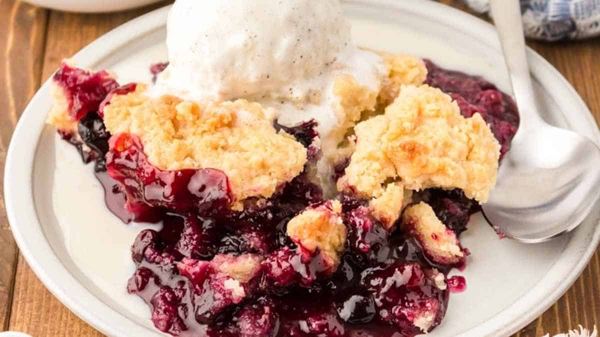 A plate of blueberry cobbler with ice cream and a scoop of ice cream.