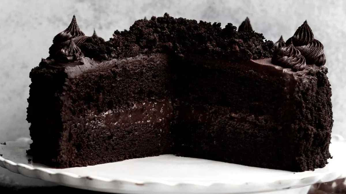 A chocolate cake on a white plate with a slice taken out.