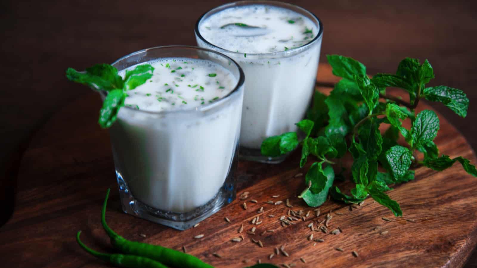 Two glasses of milk and mint on a wooden table.