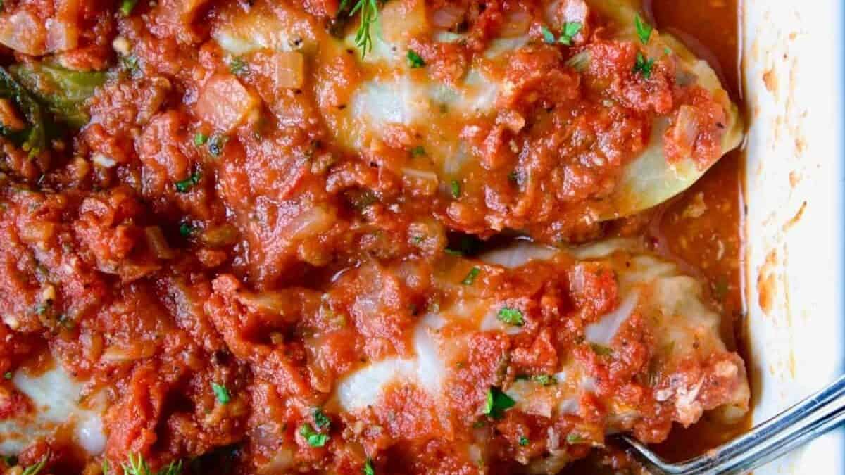Stuffed cabbage in a white baking dish with a spoon.