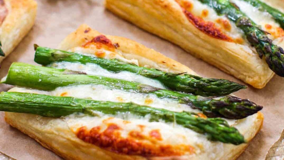 A tray of asparagus and cheese pastries on a baking sheet.
