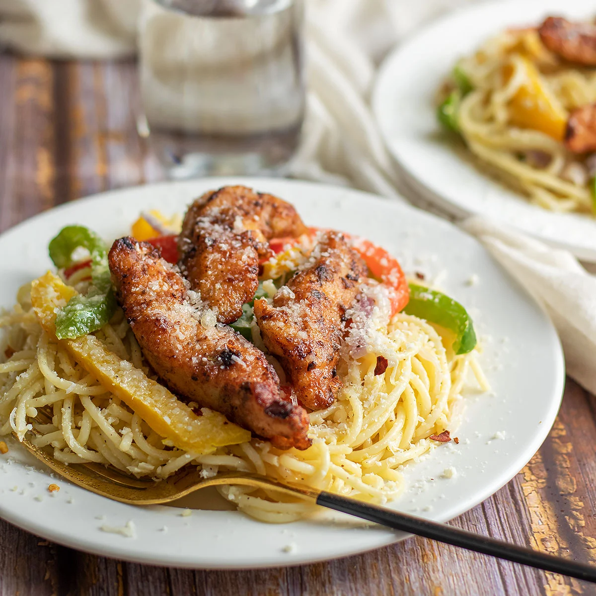 A plate of spaghetti with tender chicken and peppers on it.