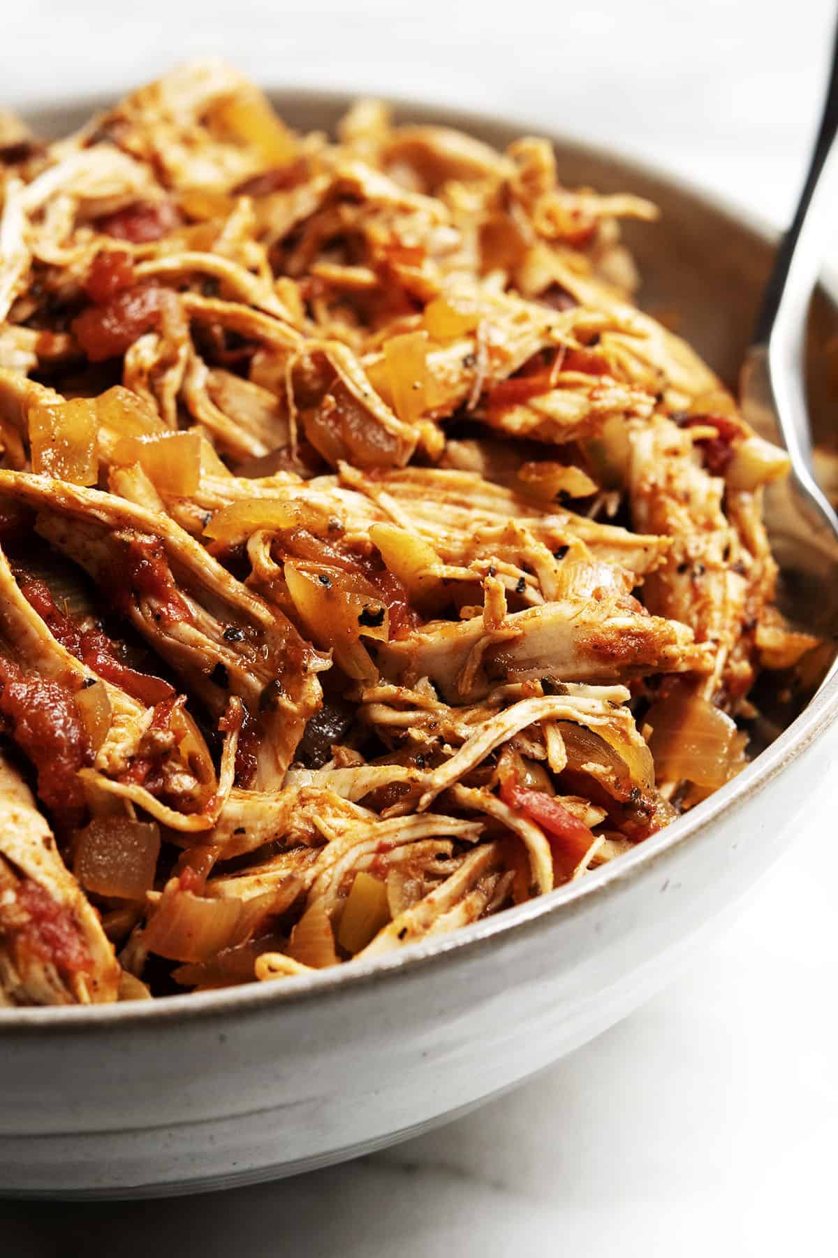 Shredded bone-in chicken breast in a white bowl with a fork.