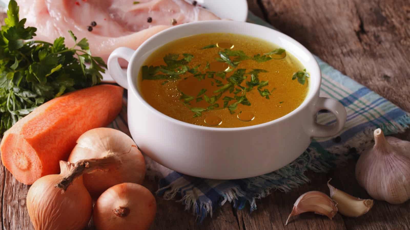 A bowl of soup with carrots, onions and garlic on a wooden table.