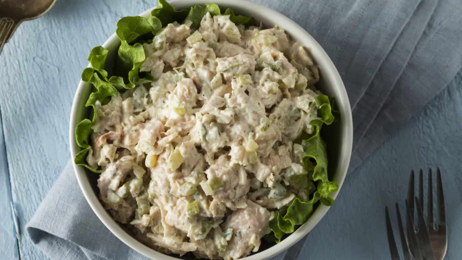A bowl of chicken salad with lettuce and forks.