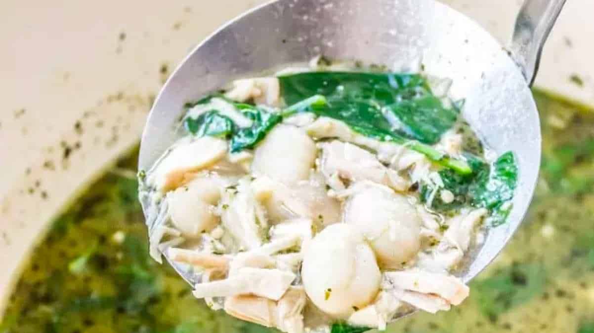 A spoon full of chicken and spinach soup.