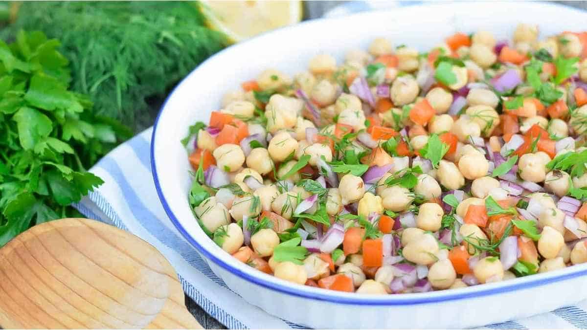 Chickpea salad in a white dish with vegetables and herbs.