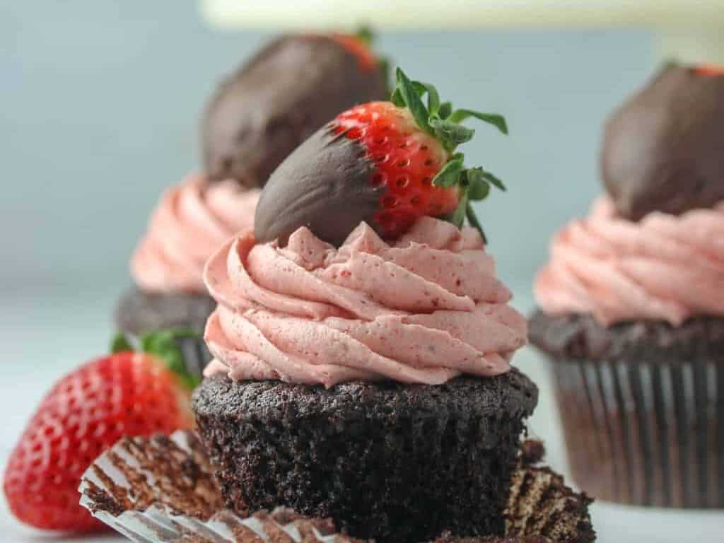 Chocolate cupcakes topped with strawberries and chocolate frosting.