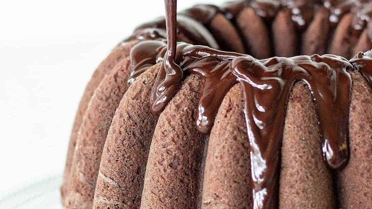 A chocolate bundt cake is being drizzled with chocolate.