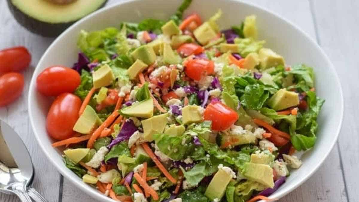 A bowl of salad with avocado, tomatoes and carrots.