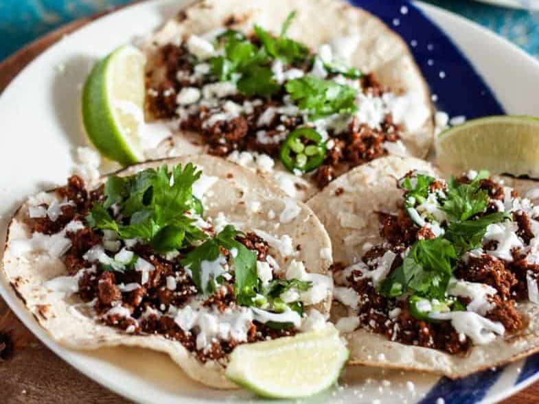 Mexican tacos on a plate with lime wedges.