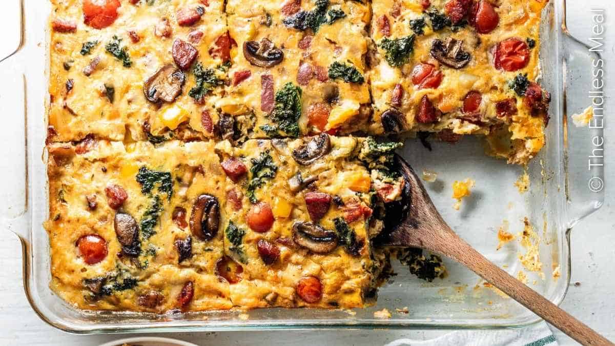 A breakfast casserole with mushrooms, spinach and tomatoes in a glass dish.