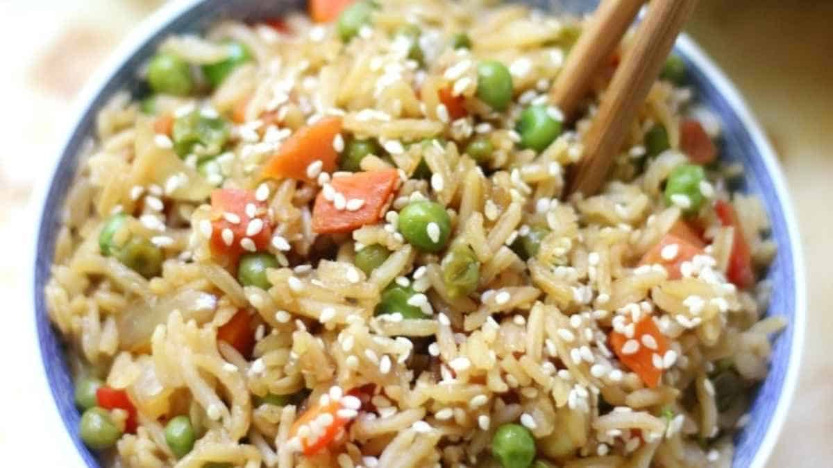 A bowl of fried rice with vegetables and chopsticks.