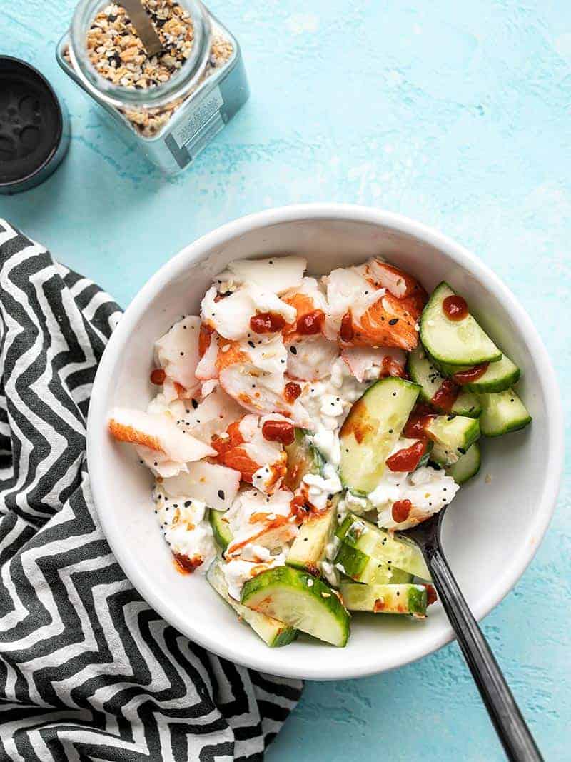 A white bowl with a refreshing cucumber salad and a spoon.