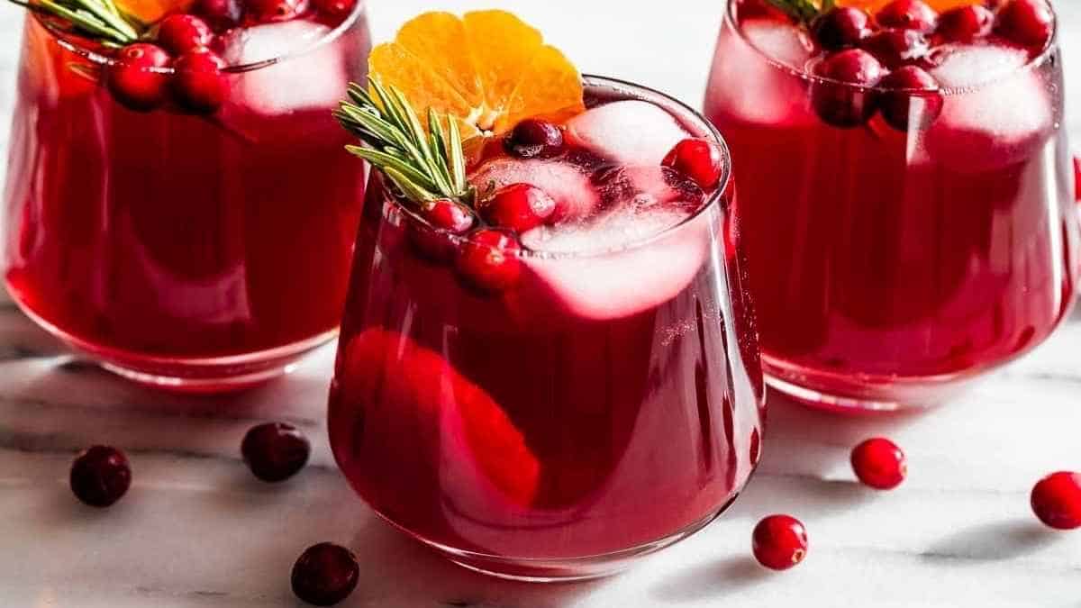Three glasses of cranberry sangria with oranges and rosemary.