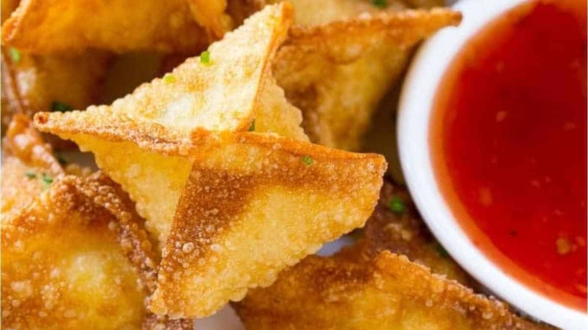 Fried wontons with dipping sauce on a white plate.