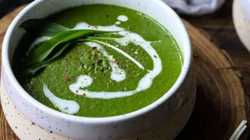 Two bowls of green soup on a wooden table.