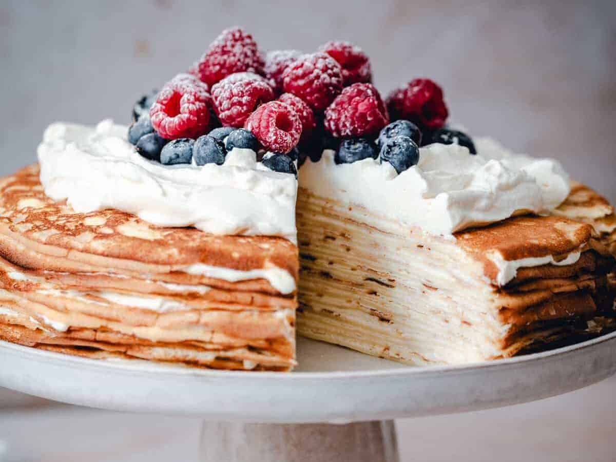 A stack of crepes with whipped cream and berries on a white plate.