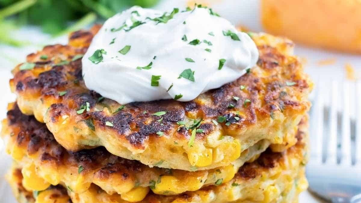 A stack of corn cakes with sour cream on top.