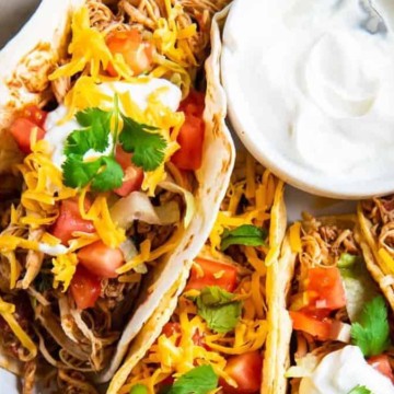 Shredded chicken tacos on a white plate with sour cream.
