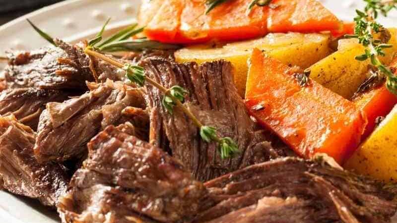 Beef roast on a plate with carrots and potatoes.
