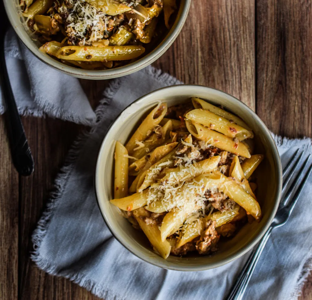 Two bowls of pasta with ground sausage and cheese.
